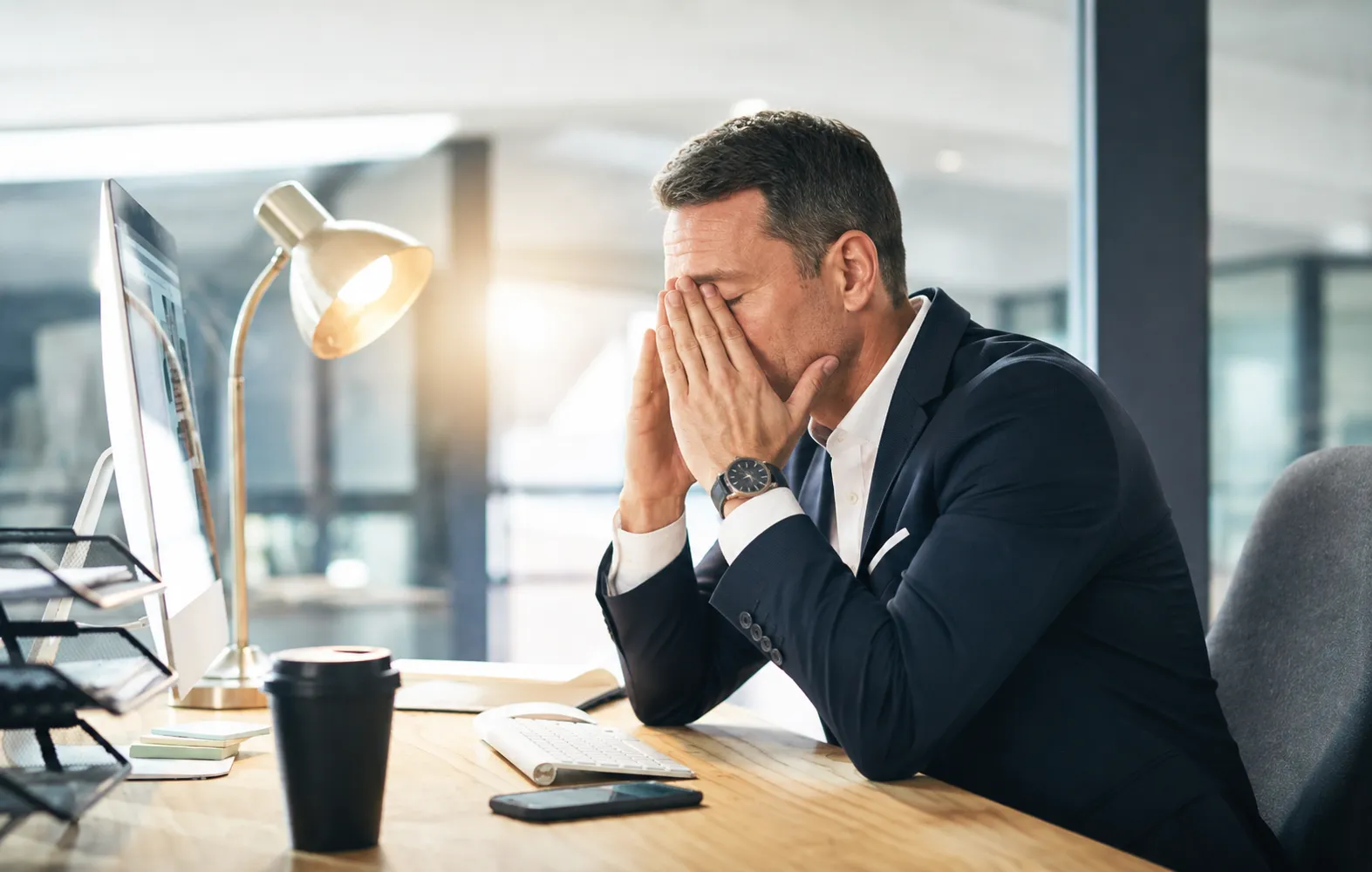 Homme d’affaires devant un écran d'ordinateur, soulageant sa fatigue oculaire en se tenant des deux mains l'arête du nez