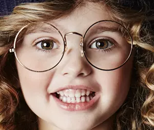 gros plan du visage d'une petite fille qui porte des lunettes rondes avec un grand sourire